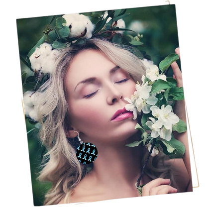 Woman with floral wreath on head surrounded by greenery and white flowers wearing ribbon pattern earrings for prostate cancer awareness.